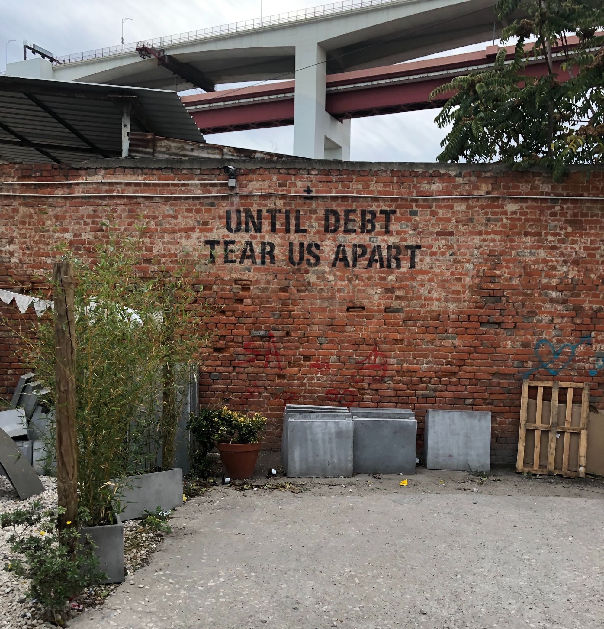 A brick wall by a highway overpass, with the words "Until debt tear us apart" written on the wall.