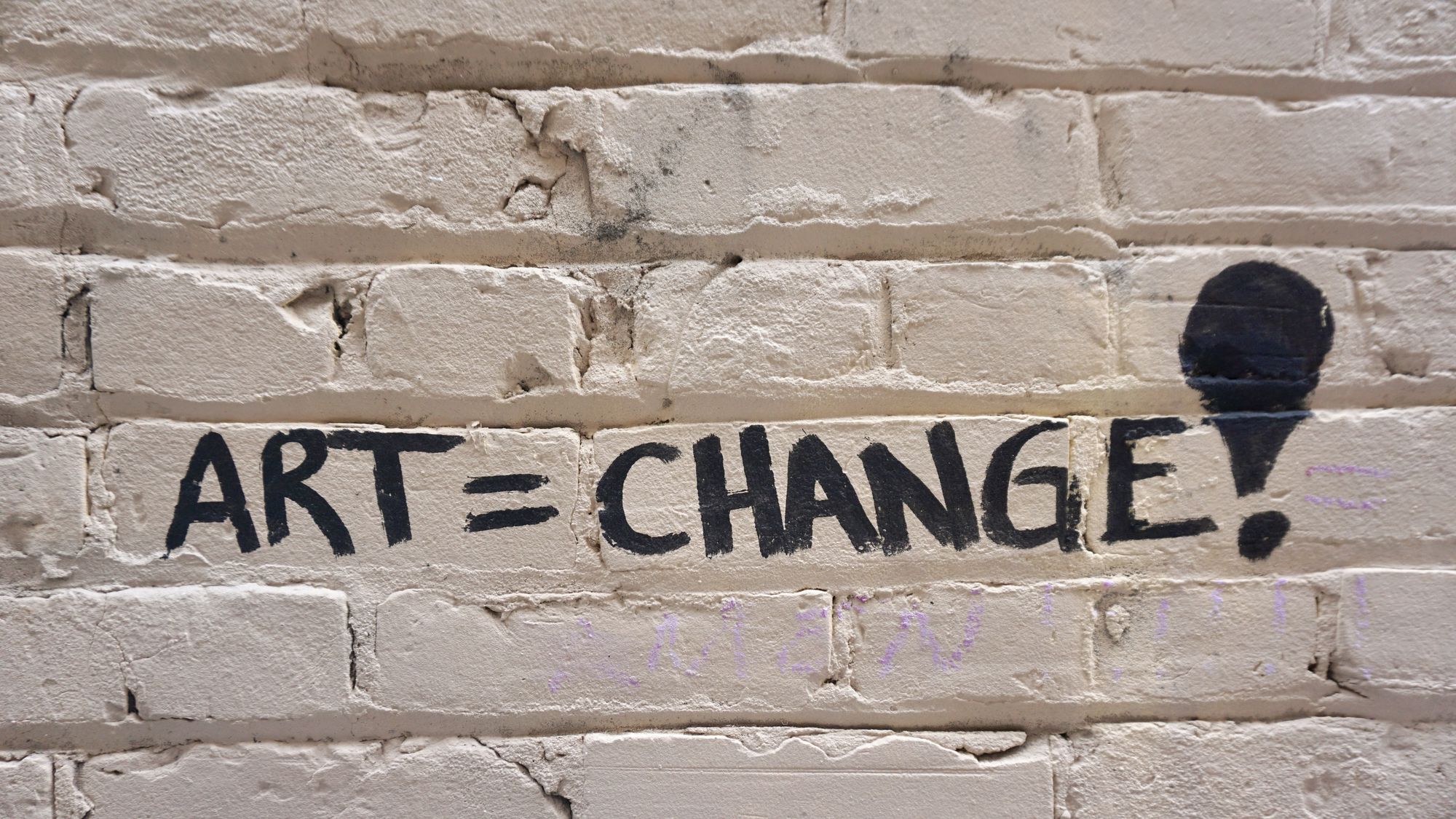 The words "art [equals] change!" written on a brick wall.