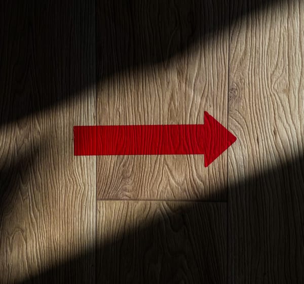 a red arrow in a stripe of light pointing to the right on a wood surface